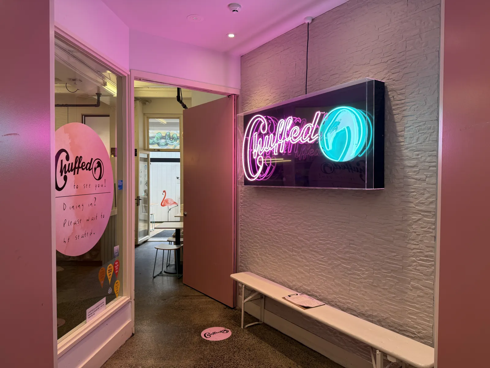 Chuffed's entrance — pink doors, handwritten welcome on the glass, and a neon Chuffed sign with flamingo